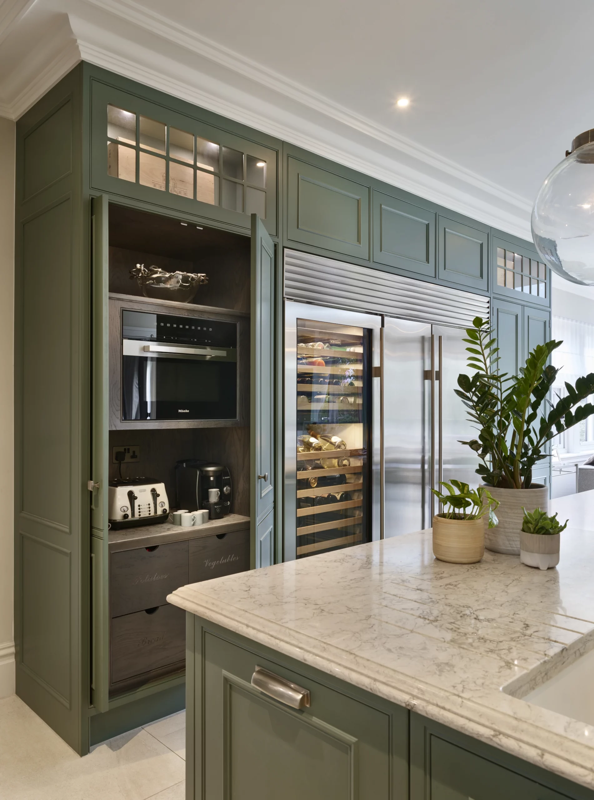 Green classic englemere kitchen with marble topped island with pocked doors for coffee station.
