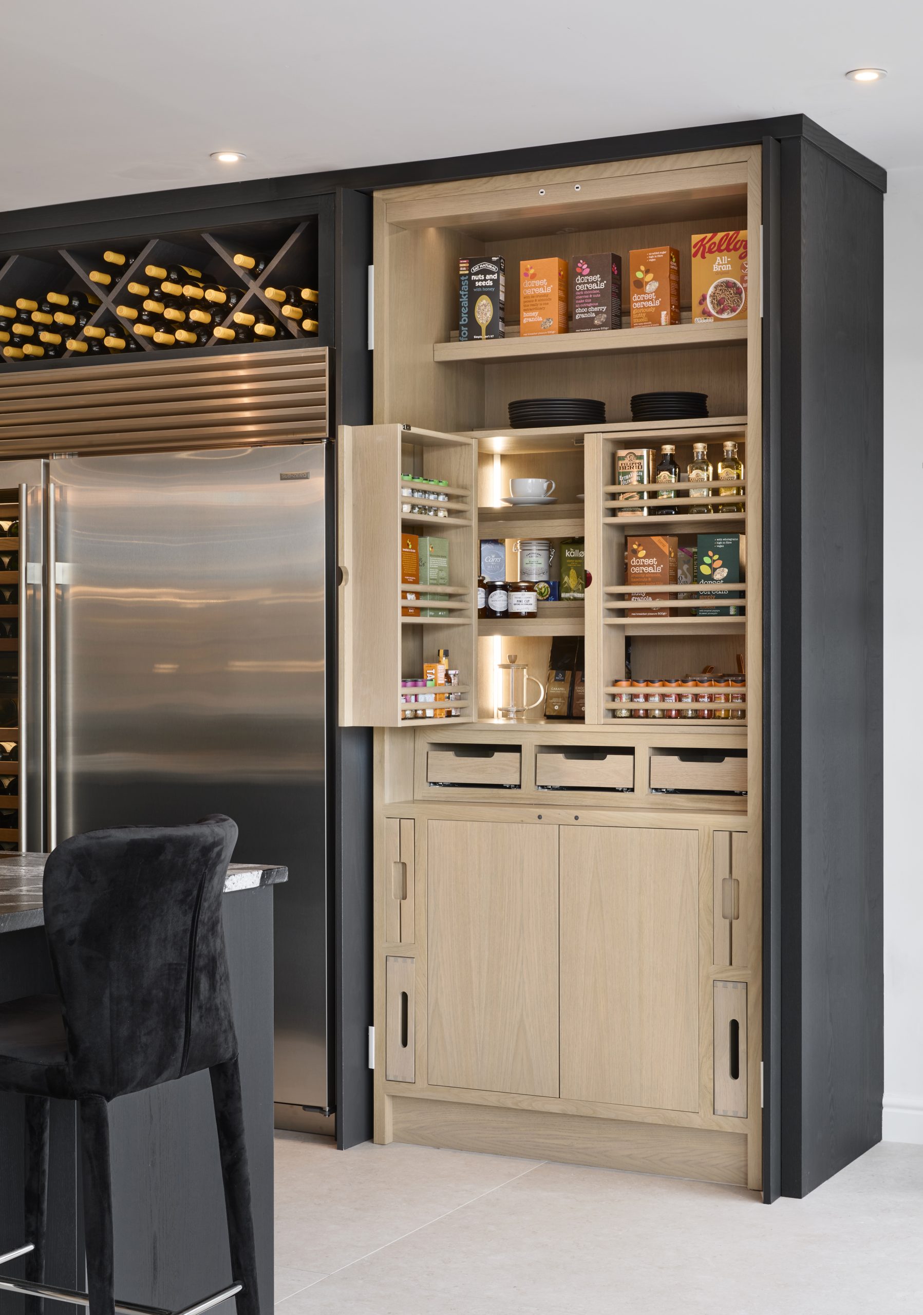Pocket door pantry in a contemporary dark Charles Yorke kitchen, with oak spice racks, pull our chopping boards and trays. 